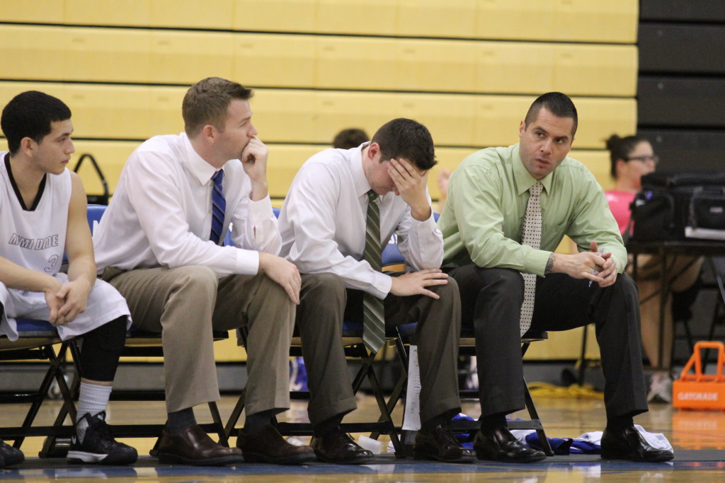 Sharks basketball coaches seated on the bench.